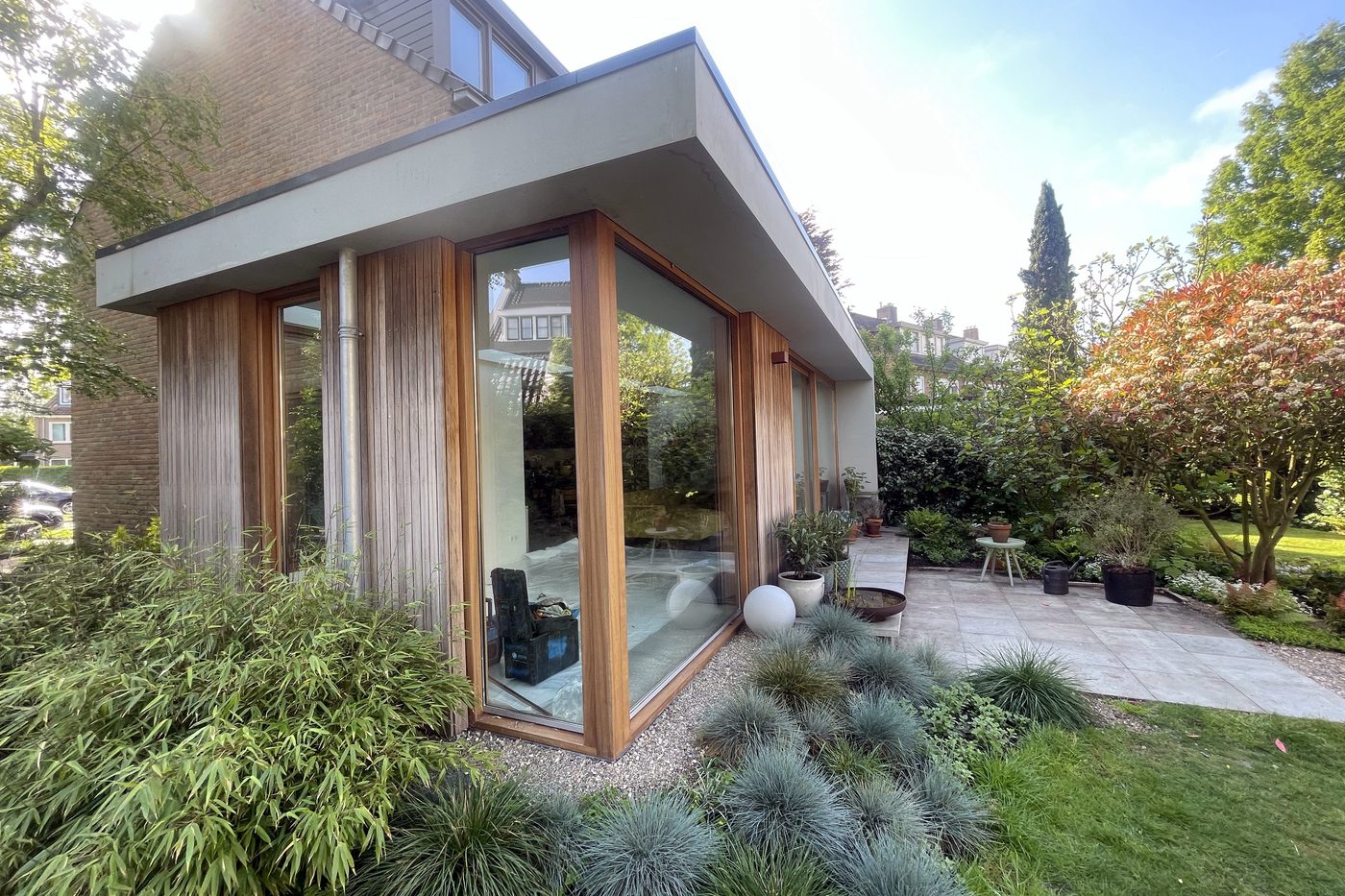 Aanbouw met houten glaspui en strak dakoverstek in een groene tuin