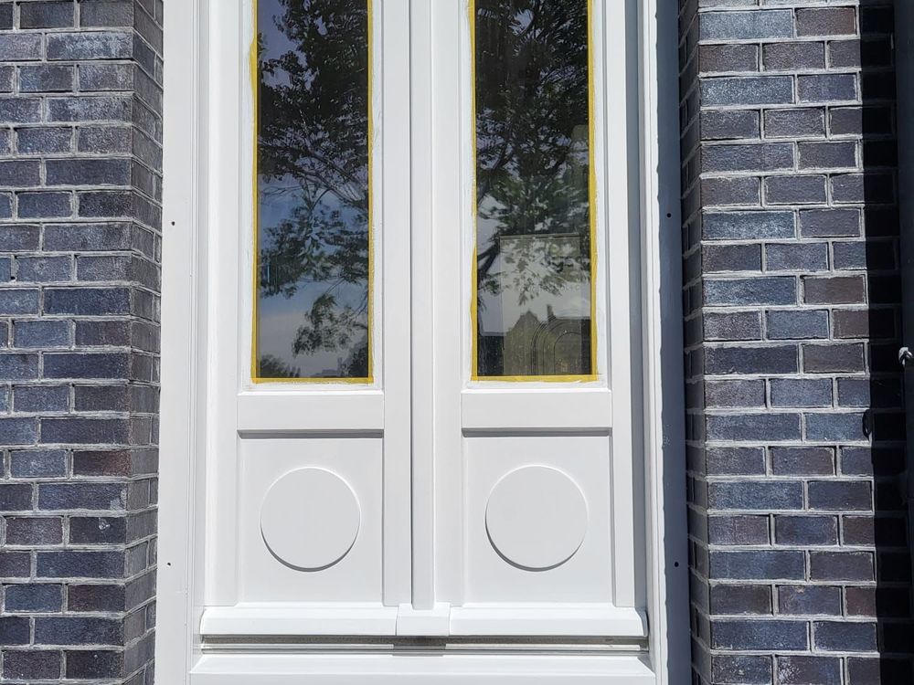 Wit gelakte dubbele deur met ronde panelen in een donkere bakstenen gevel