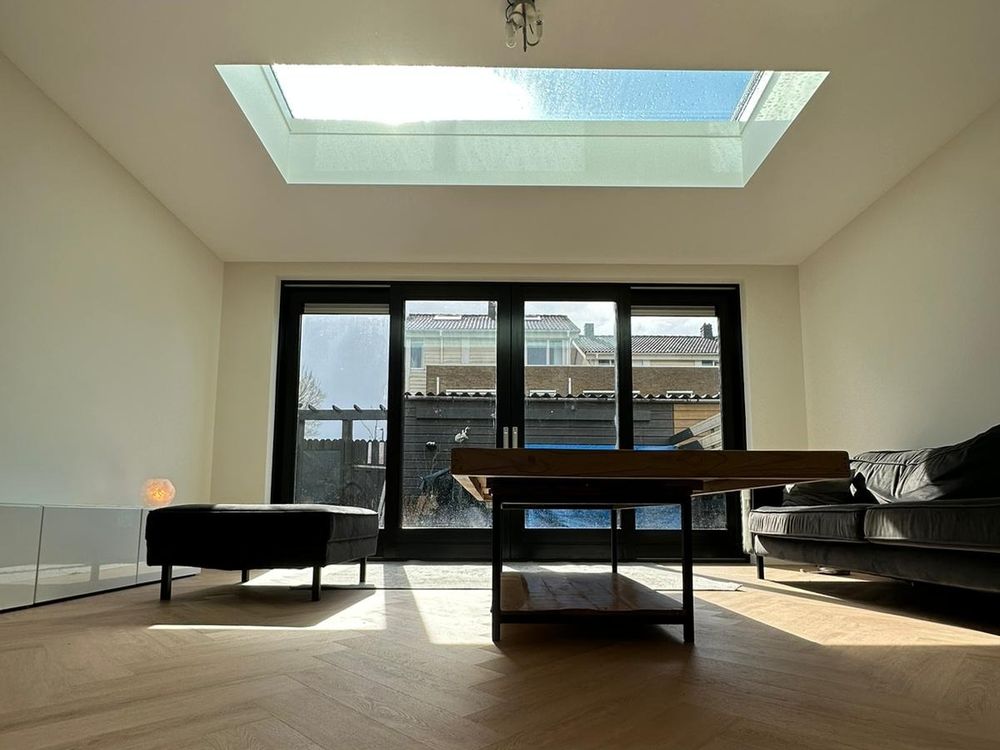 Woonkamer met lichtstraat, visgraatvloer en zwarte pui naar de tuin