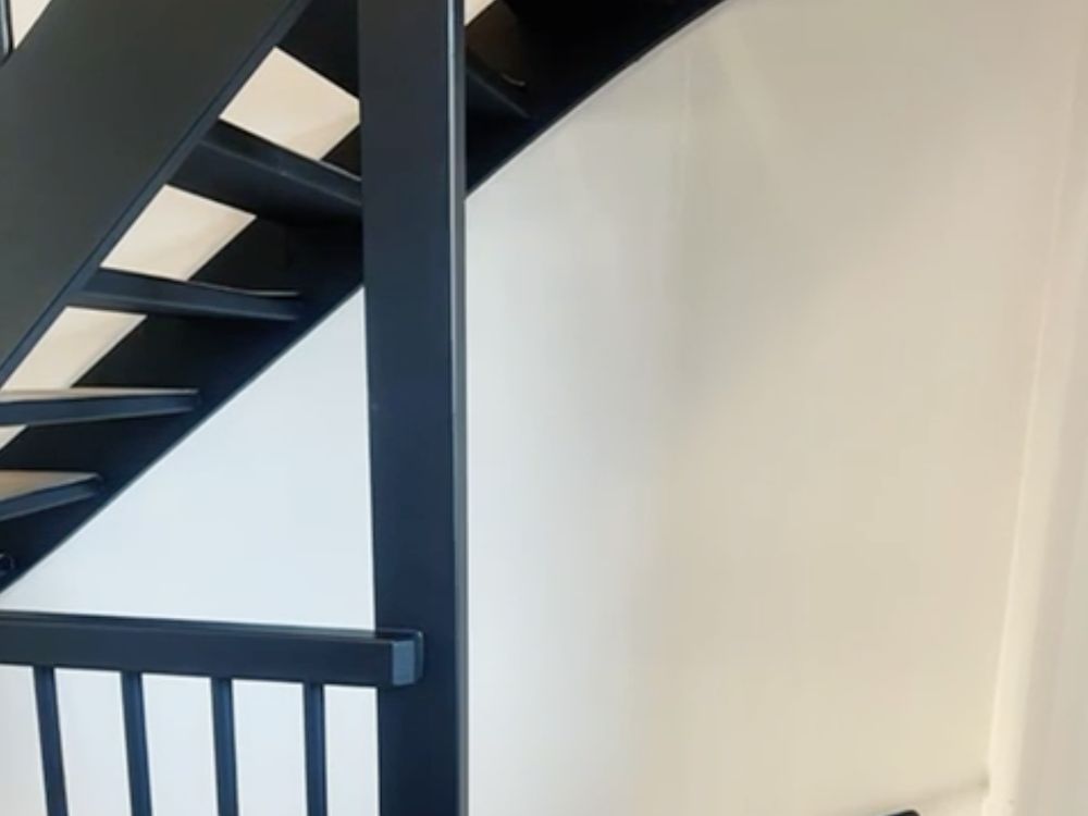 Trapgat met zwarte trap en spijlen, strak gestuukte wand
