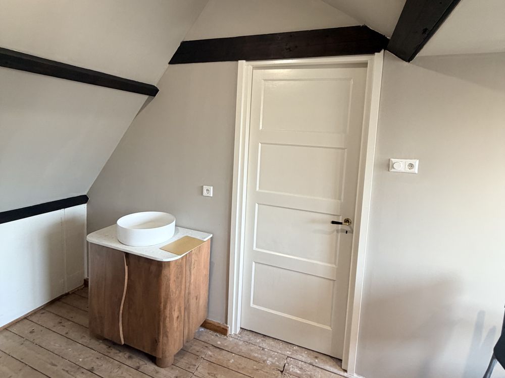 Gerenoveerde zolderkamer met zichtbare balken, paneeldeur en wastafel